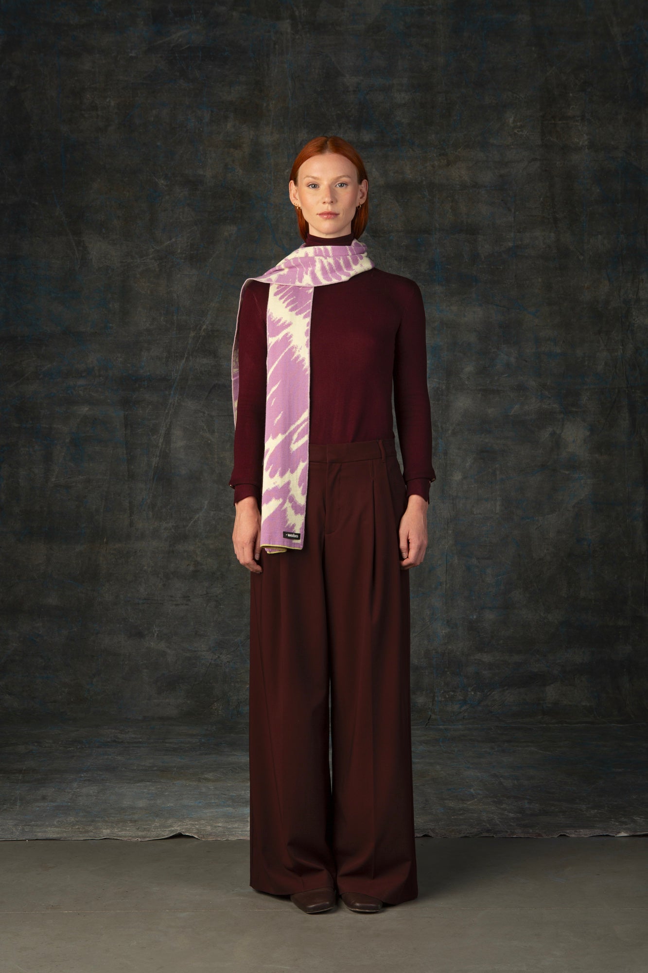 Female model wearing a burgundy outfit with a pink and beige midi scarf, with an organic pattern, draped around her neck.