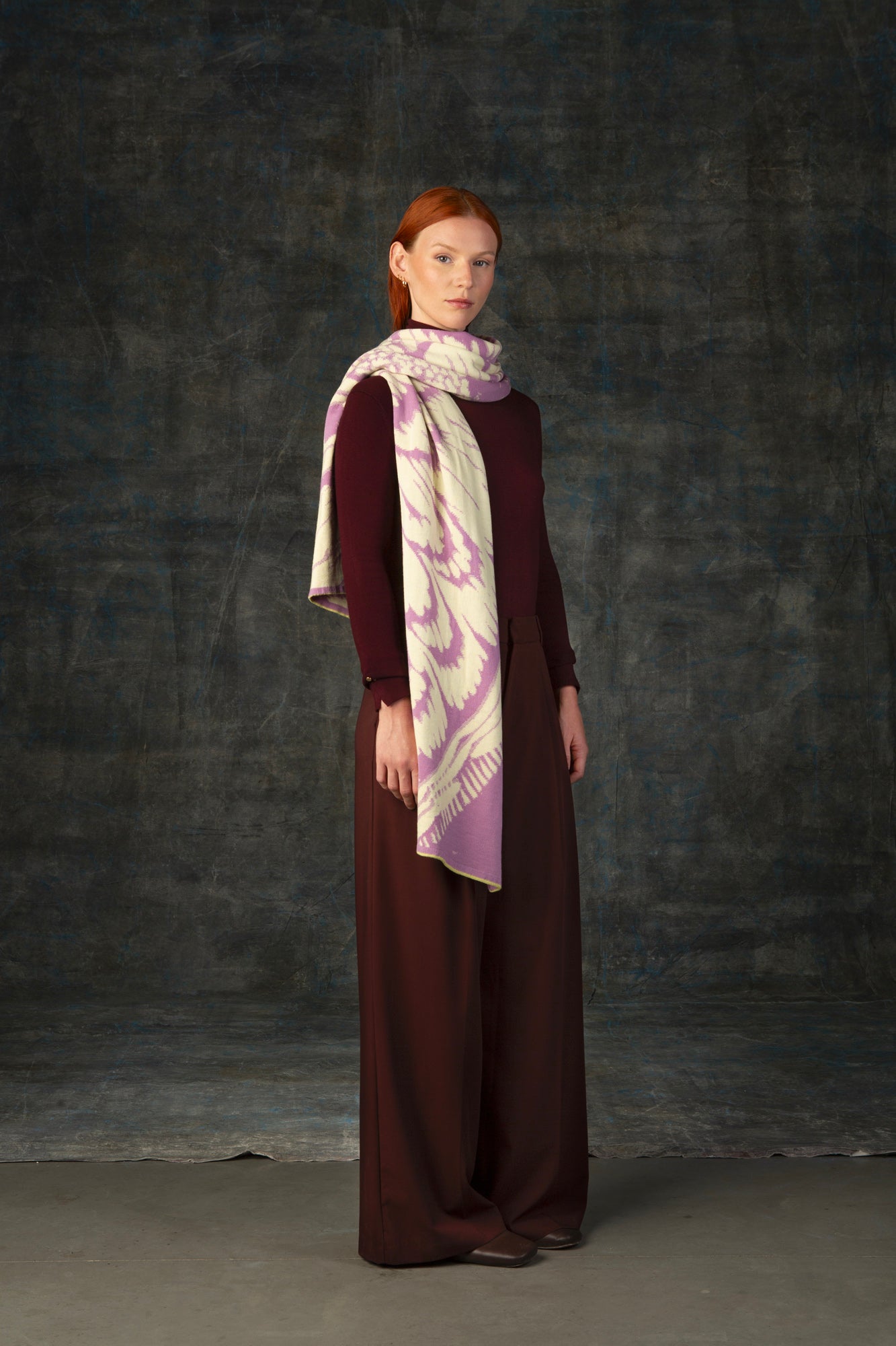Female model wearing a burgundy outfit with a pink and beige maxi scarf, with an organic pattern, draped around her neck.