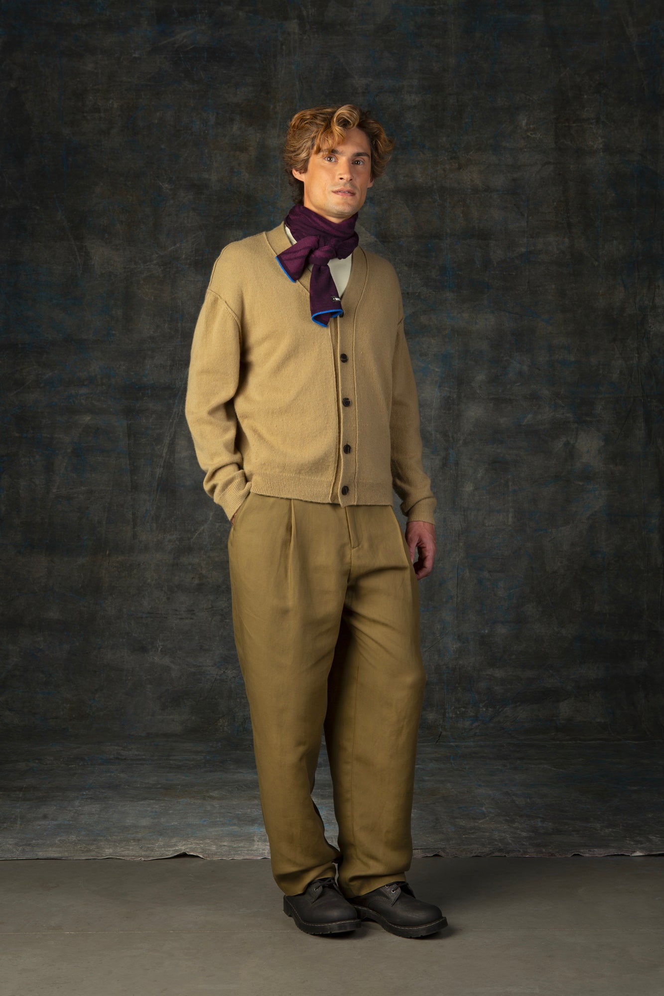 Male model wearing a muted mustard yellow outfit with a dark purple mini scarf, with nature-inspired pattern closely tied around his neck.