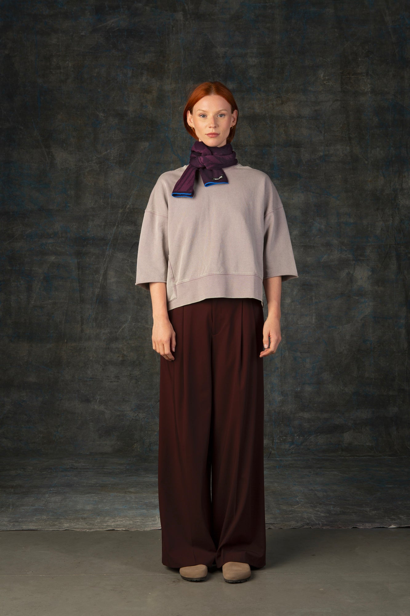 Female model wearing a neutral outfit with a dark purple mini scarf, with nature-inspired pattern closely tied around her neck.