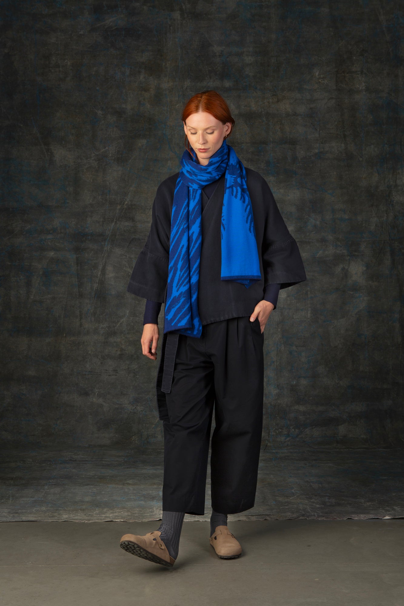 Female model wearing a dark blue outfit with a bright cobalt blue scarf, with nature-inspired pattern, draped around her neck.