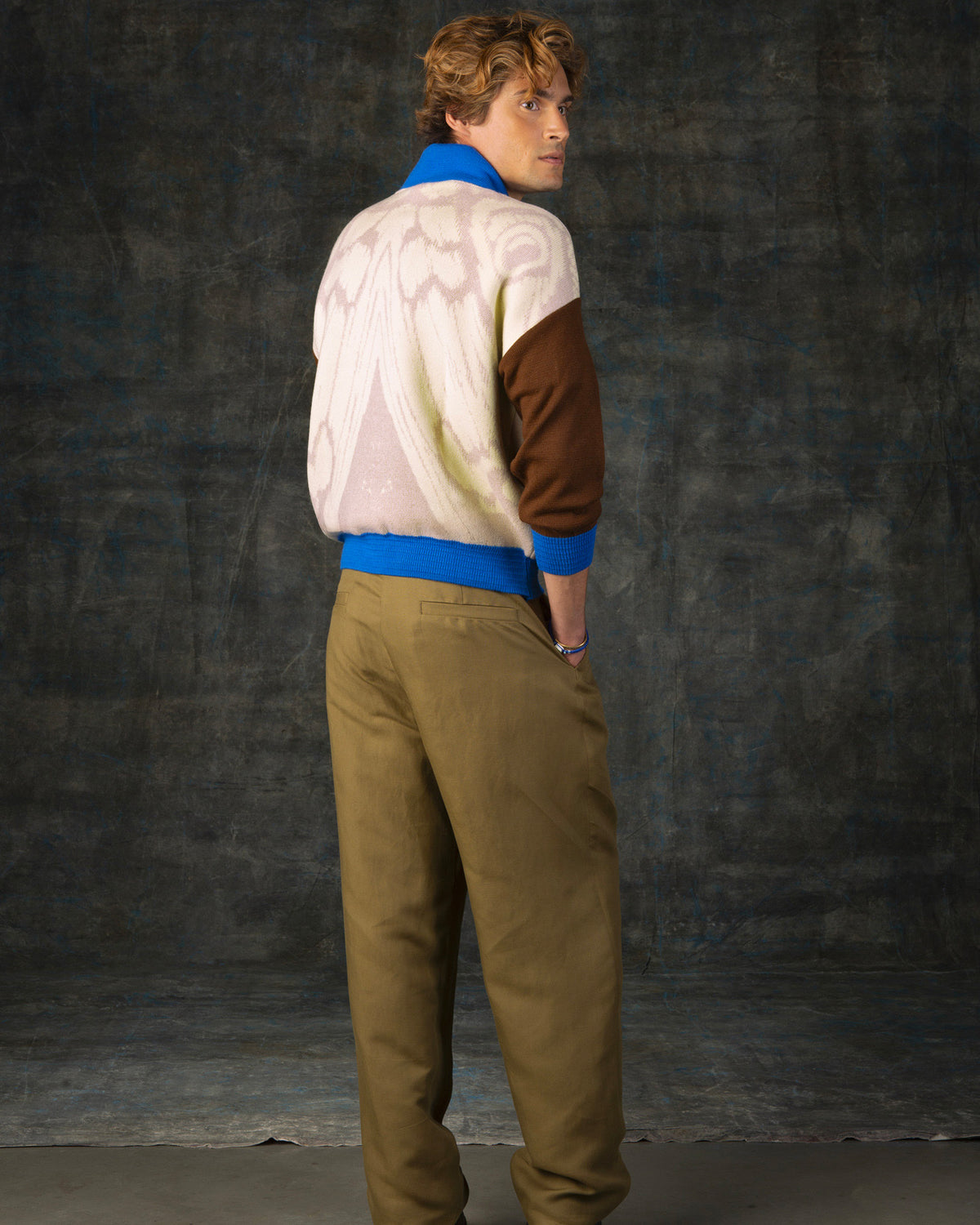 Male model facing away from the camera wearing an ecru and brown bomber jacket with cobalt blue details. There is a subtle organic pattern inspired by a butterfly's wings on the back of the jacket.