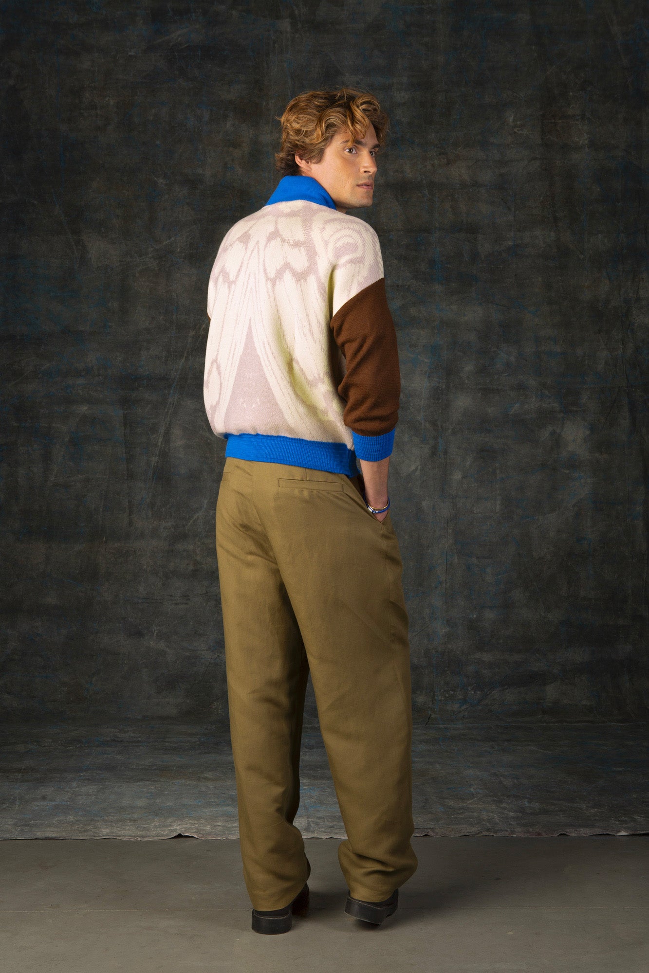 Male model facing away from the camera wearing an ecru and brown bomber jacket with cobalt blue details. There is a subtle organic pattern inspired by a butterfly's wings on the back of the jacket.