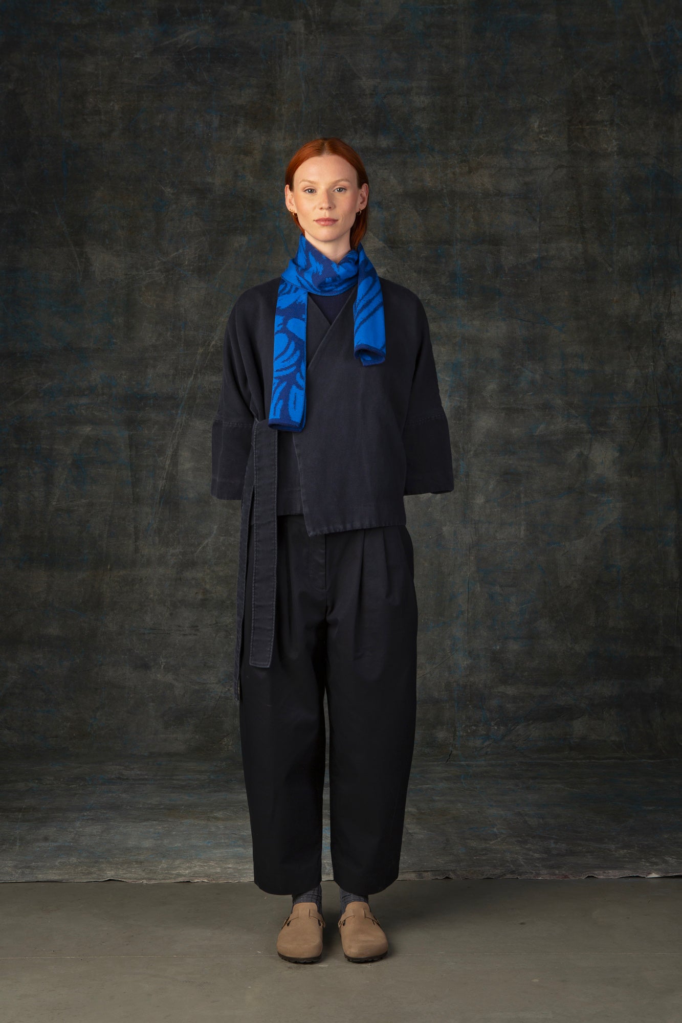 Female model wearing a dark blue outfit with a bright cobalt blue mini scarf, with organic pattern, draped around her neck.