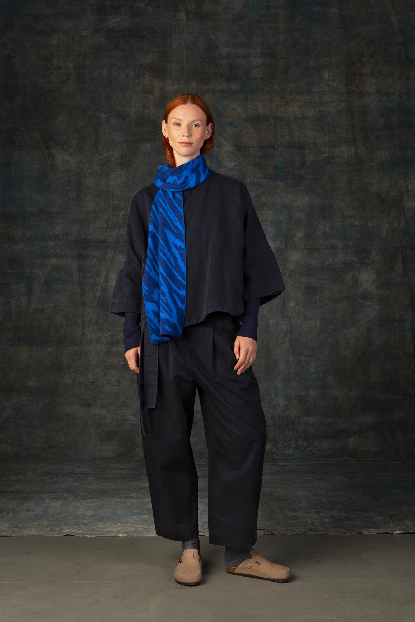 Female model wearing a dark blue outfit with a bright cobalt blue midi scarf, with organic pattern, draped around her neck.