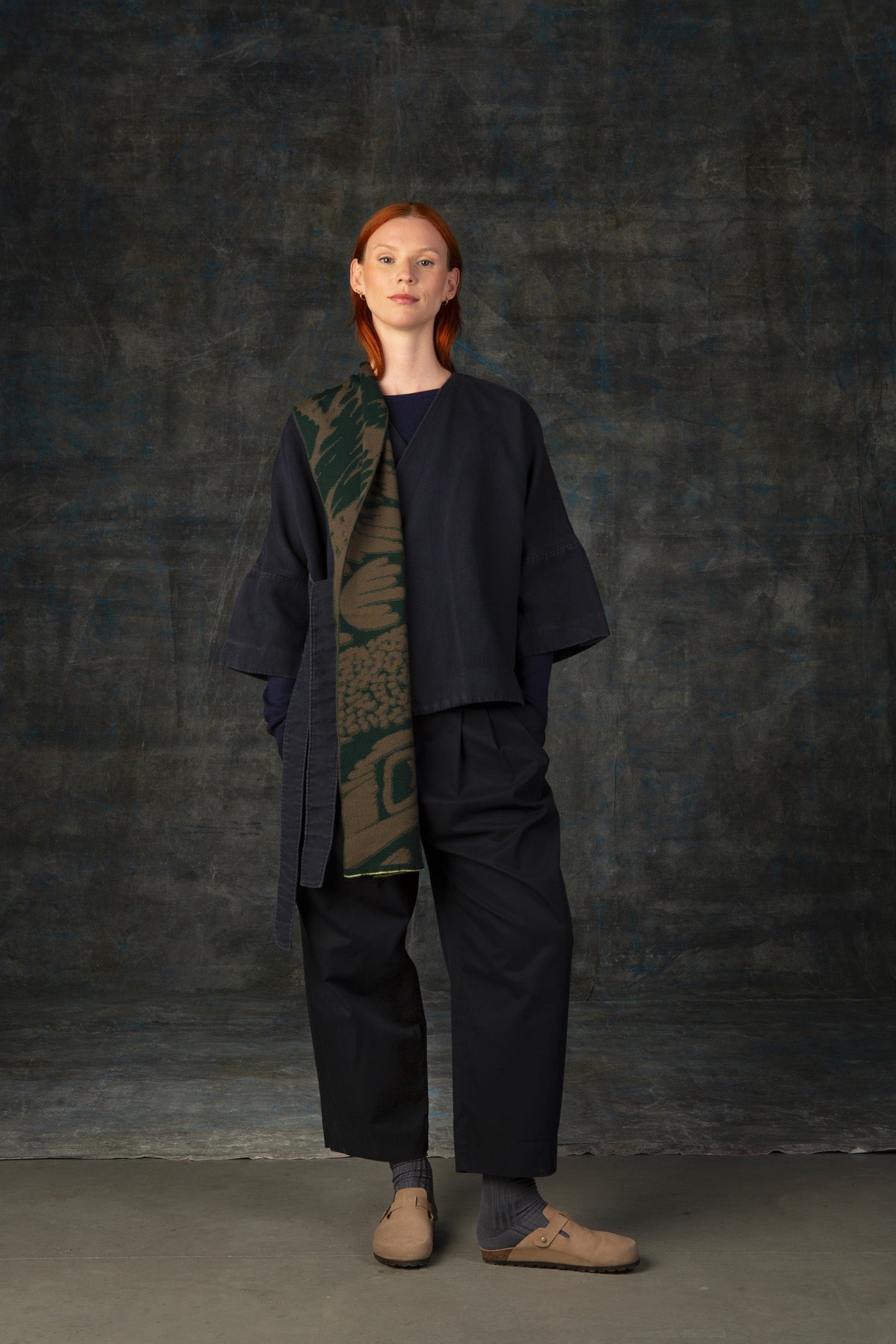 Female model wearing a dark blue outfit with a green and olive midi scarf, with an organic pattern, draped over her shoulder.