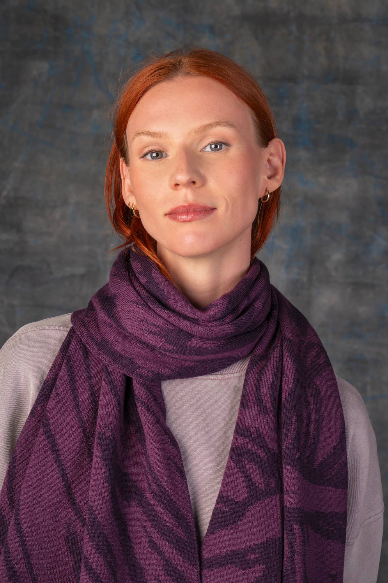Close up of a female model wearing a neutral outfit with a dark purple maxi scarf, with nature-inspired pattern draped around her neck.