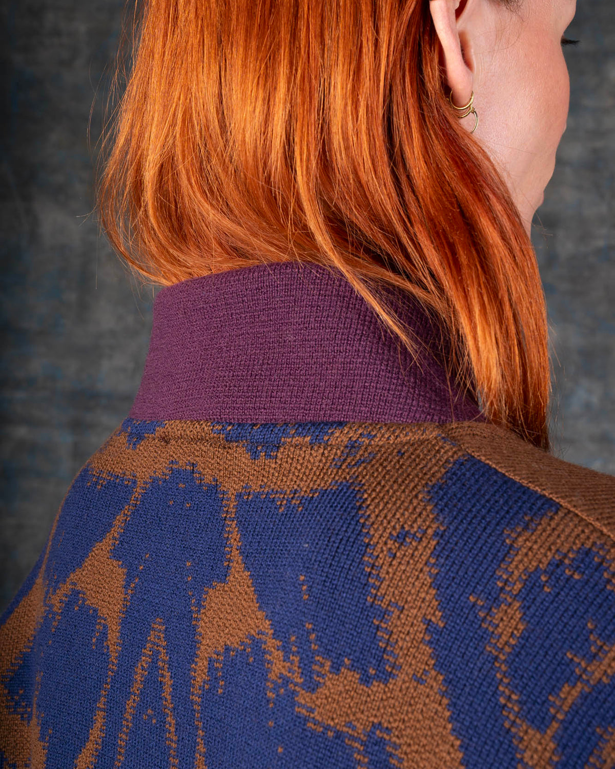 Close-up of a person wearing a brown bomber jacket with dark blue sleeves and purple collar. There is an organic pattern inspired by a butterfly's wings on the back of the jacket.