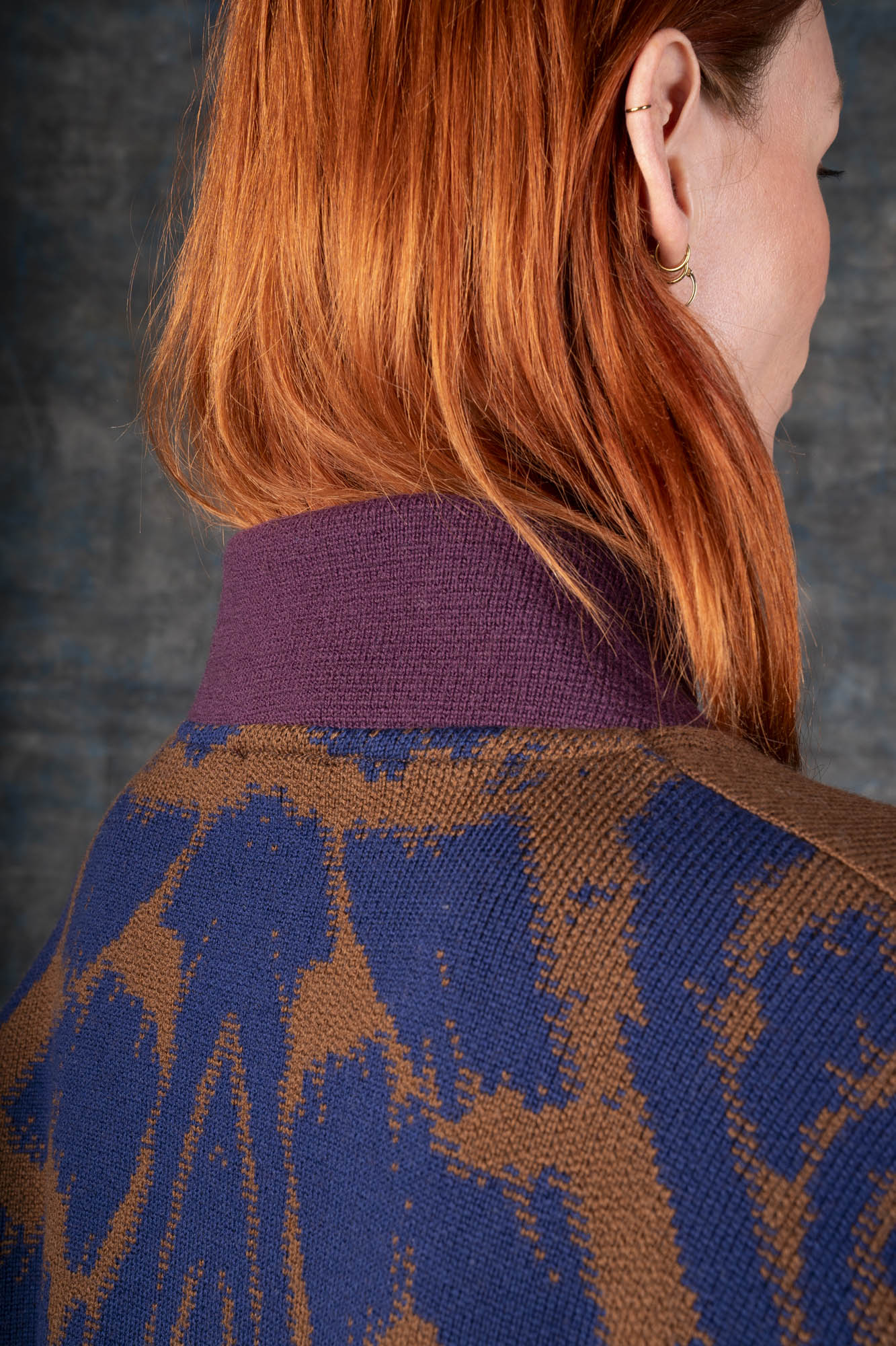 Close-up of a person wearing a brown bomber jacket with dark blue sleeves and purple collar. There is an organic pattern inspired by a butterfly's wings on the back of the jacket.