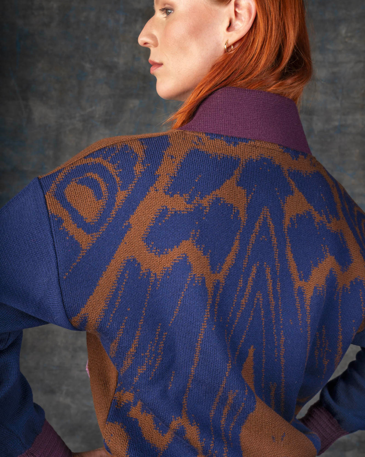 Close-up of a person wearing a brown and dark blue bomber jacket. There is an organic pattern inspired by a butterfly's wings on the back of the jacket.