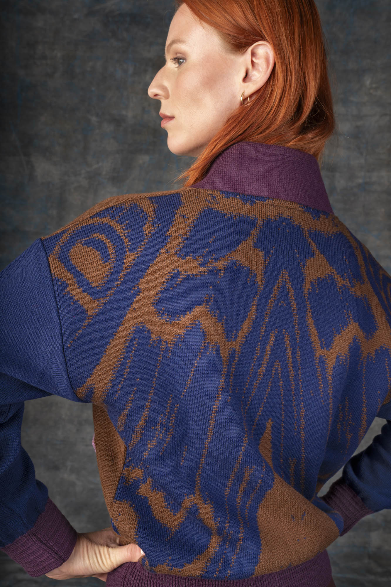 Close-up of a person wearing a brown and dark blue bomber jacket. There is an organic pattern inspired by a butterfly's wings on the back of the jacket.