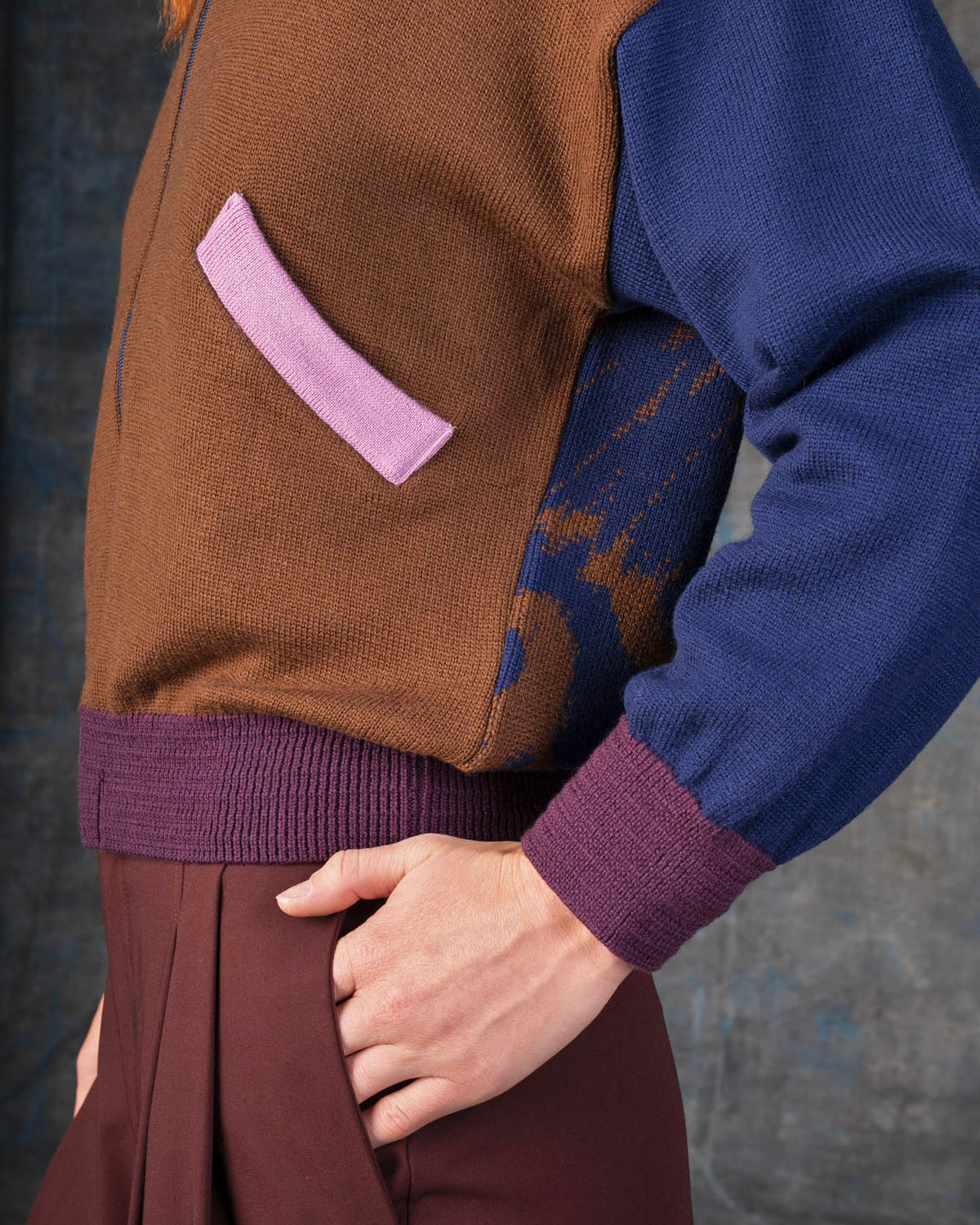 Close-up of a person wearing a brown zip-up bomber jacket with dark blue sleeves and purple cuffs.