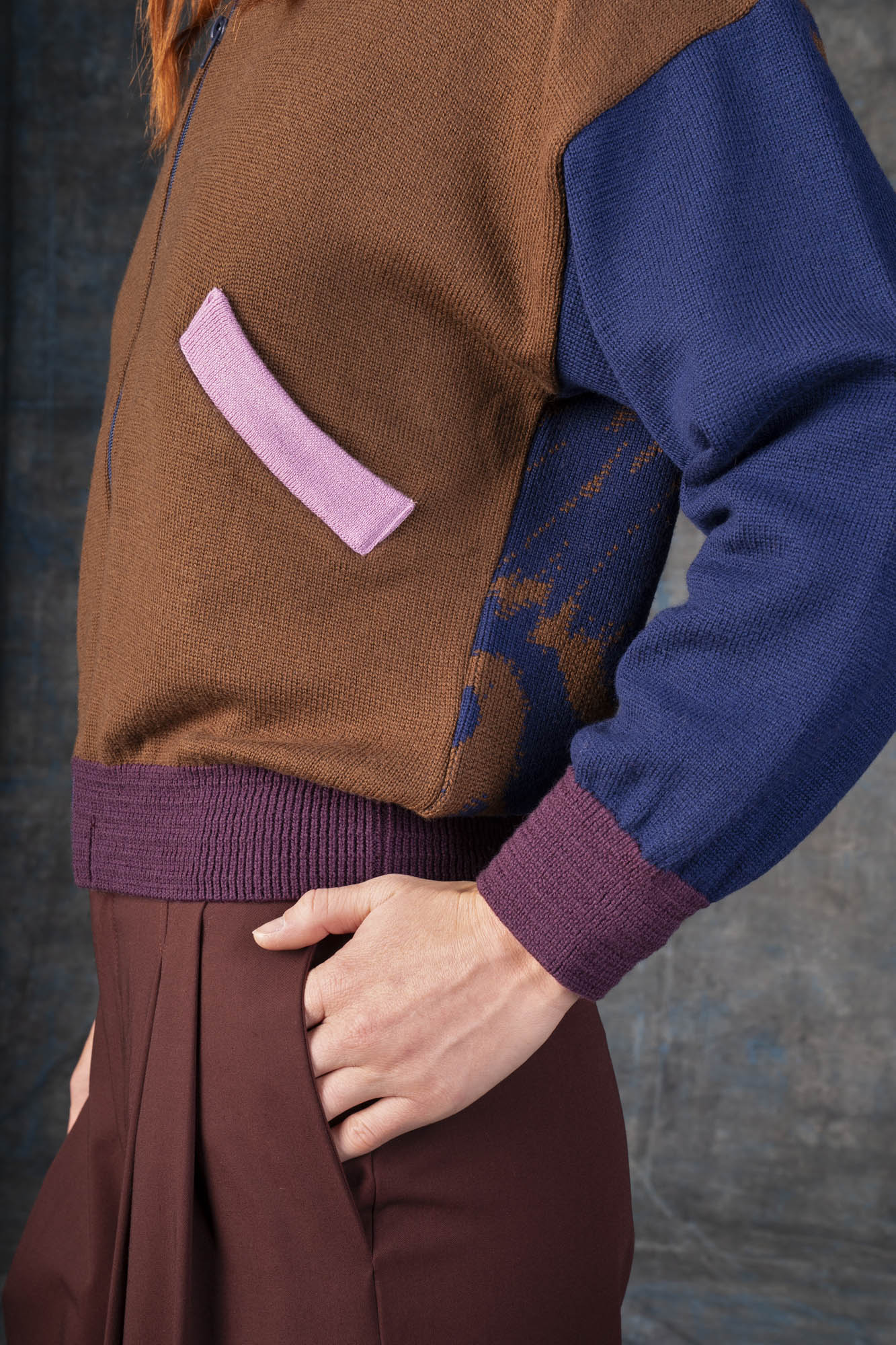Close-up of a person wearing a brown zip-up bomber jacket with dark blue sleeves and purple cuffs.