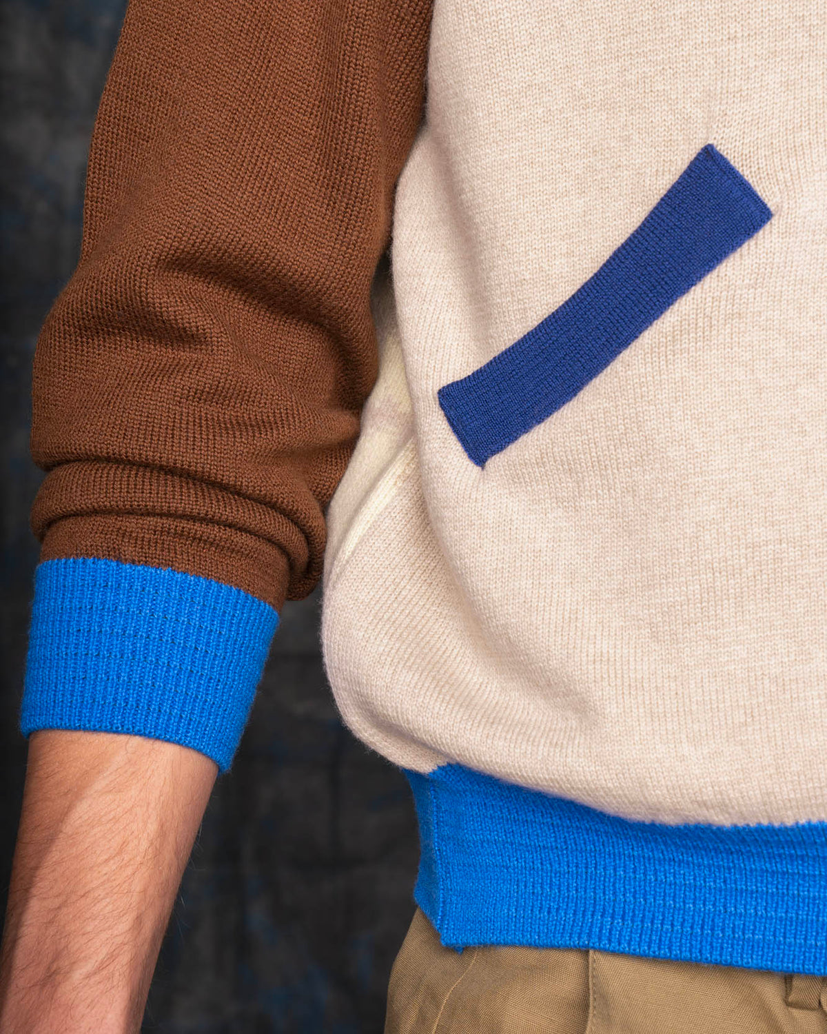 Close-up of a person wearing an ecru bomber jacket with brown sleeves and cobalt blue cuffs.