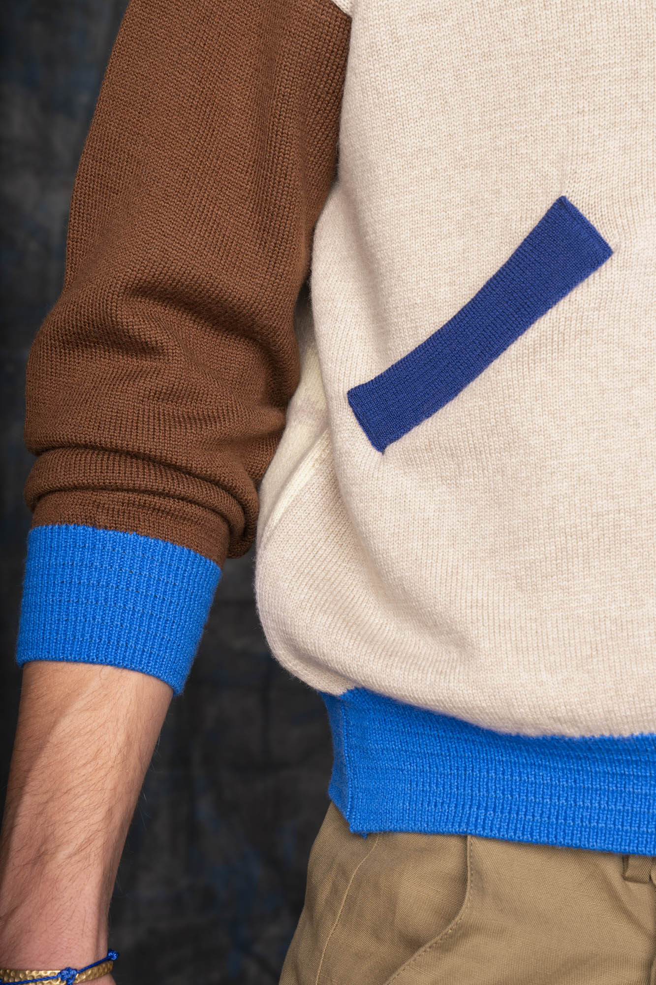 Close-up of a person wearing an ecru bomber jacket with brown sleeves and cobalt blue cuffs.