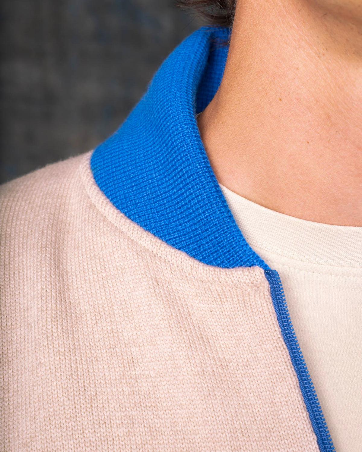 Close-up of a person wearing an ecru zip-up bomber jacket with a cobalt blue collar and zipper.