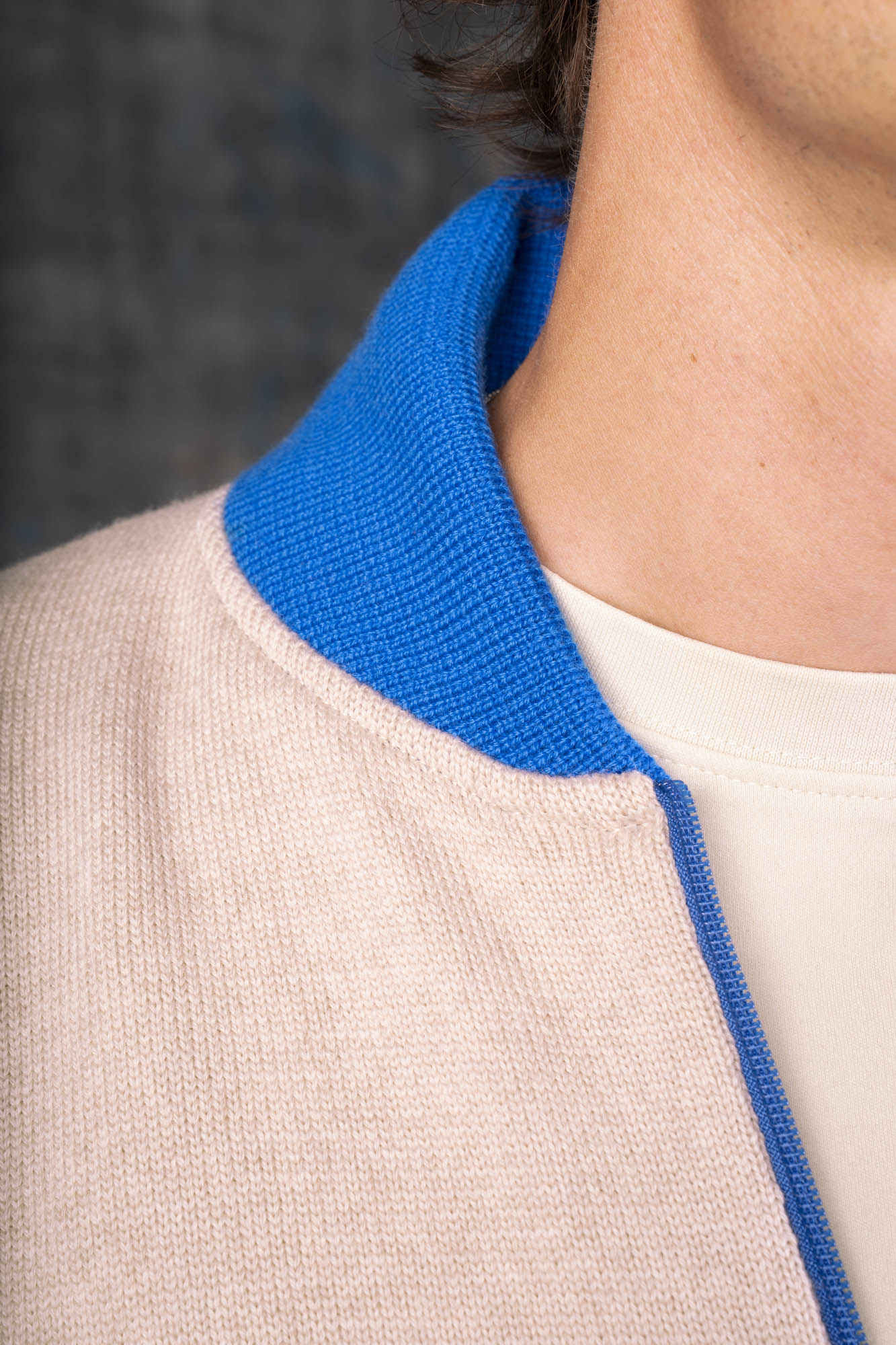 Close-up of a person wearing an ecru zip-up bomber jacket with a cobalt blue collar and zipper.