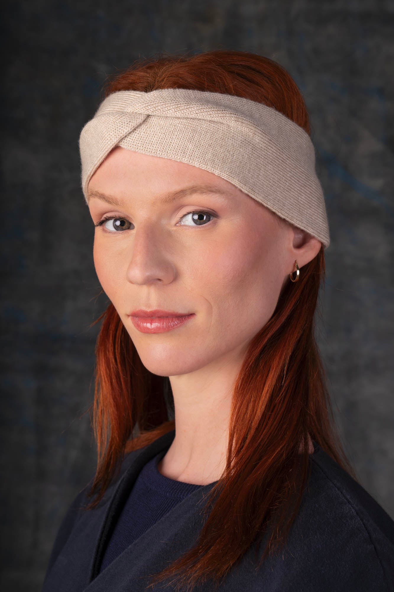 Person wearing an ecru knit headband and dark blue coat against a dark background.
