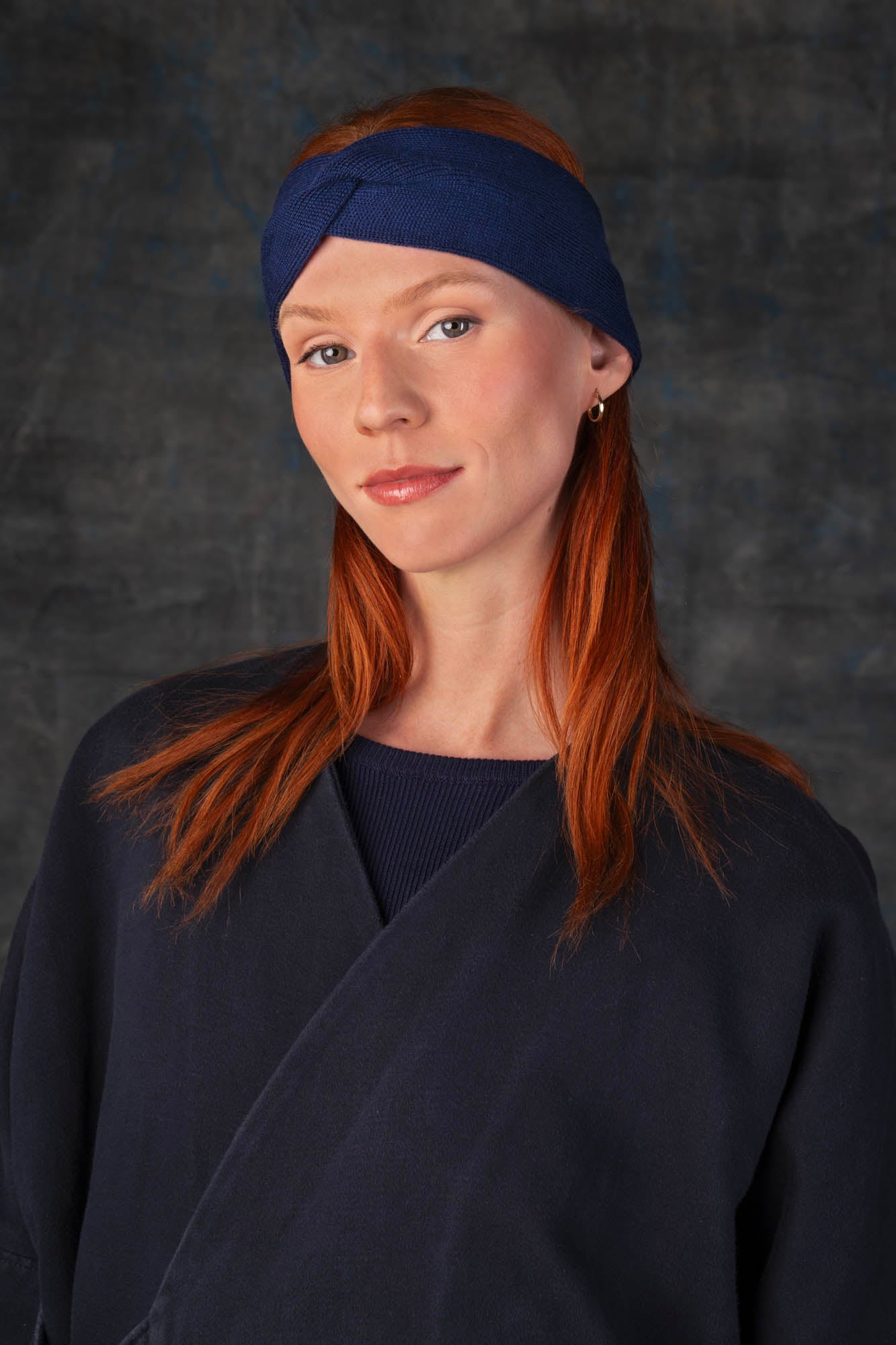 Person wearing a dark blue knit headband and dark blue coat against a dark background.