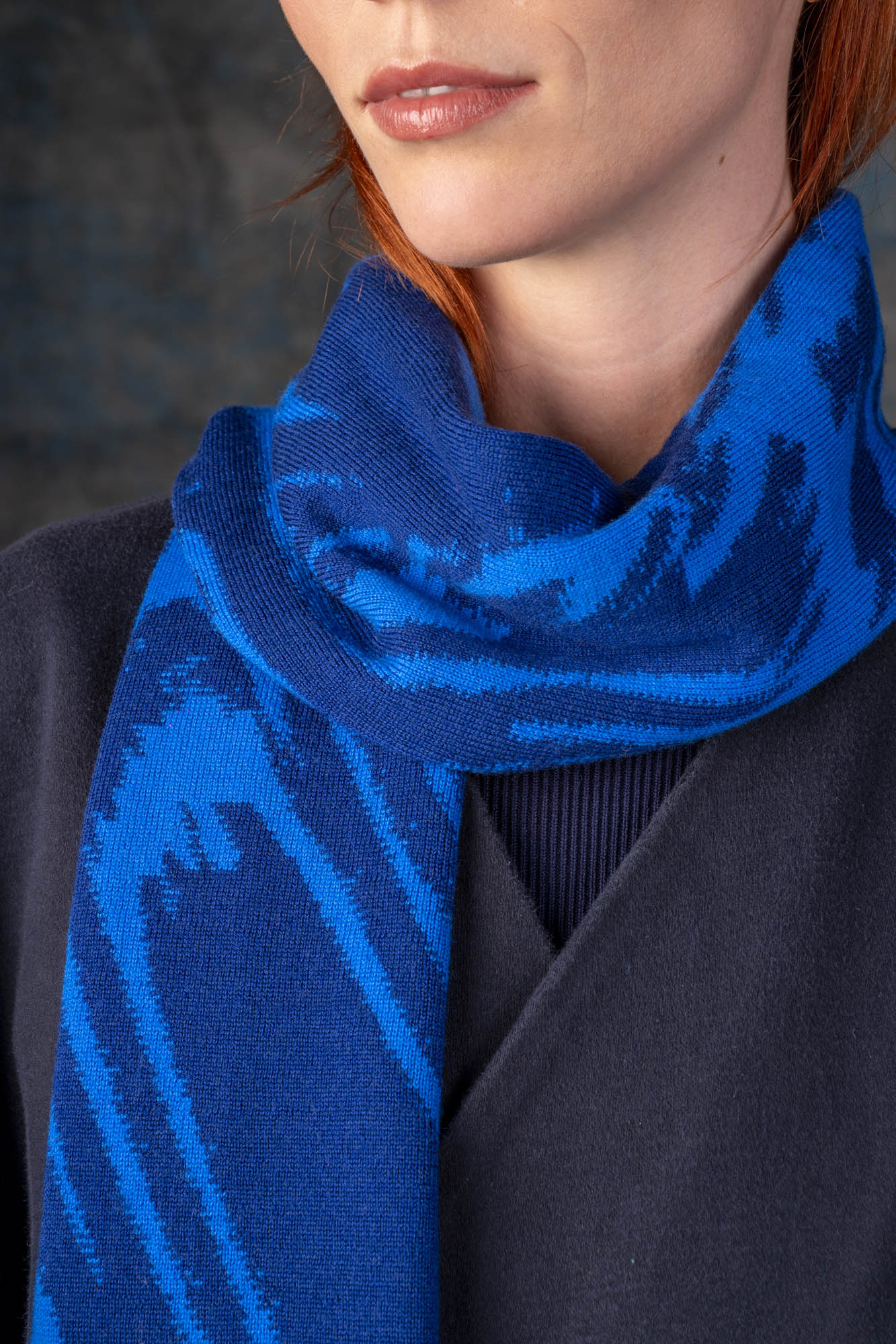 Close-up of a female model wearing a dark blue jacket with a bright cobalt blue midi scarf, with organic pattern, draped around her neck.