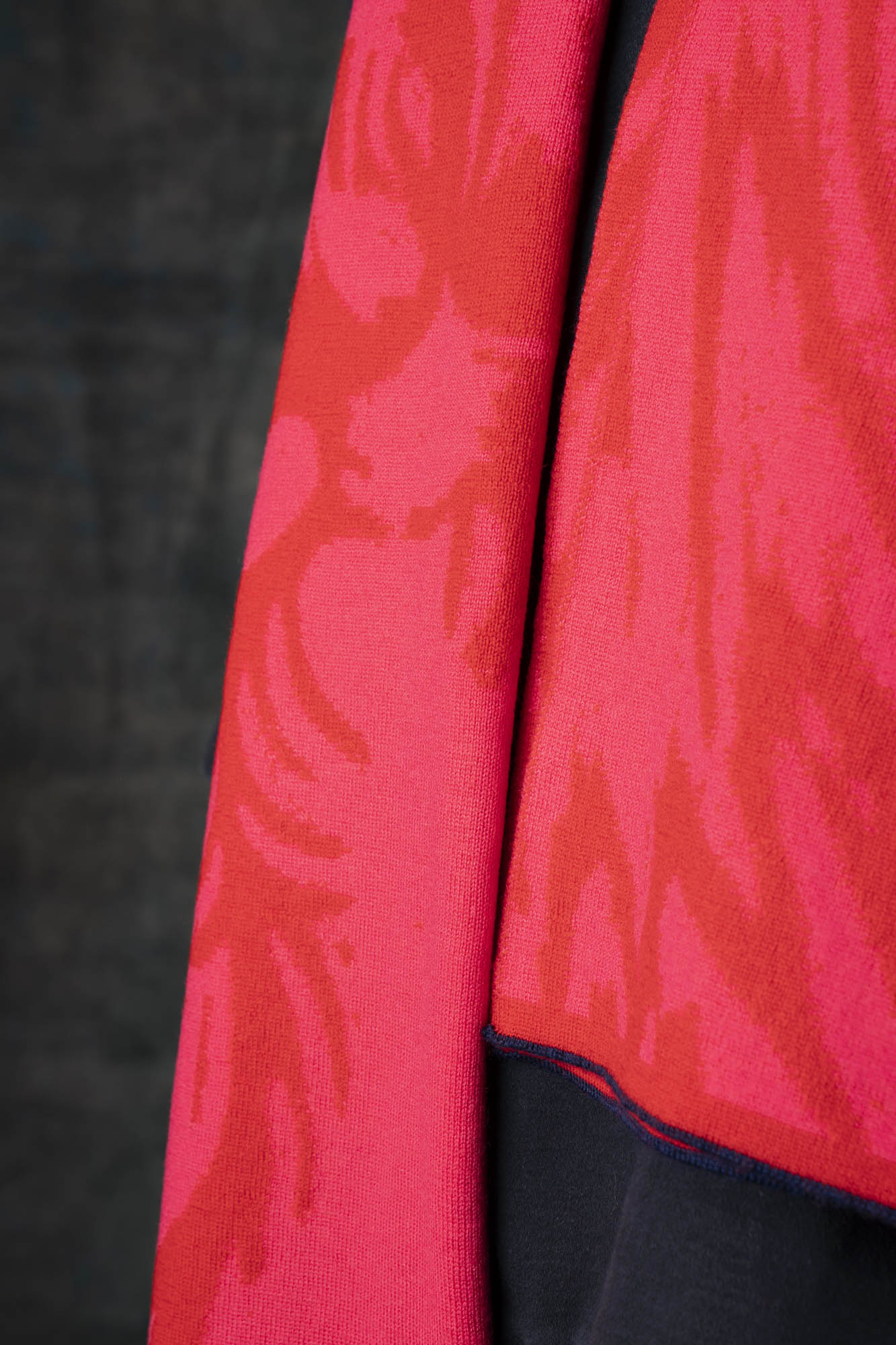 Close-up of a bright red and pink scarf with a nature-inspired pattern against a dark background.