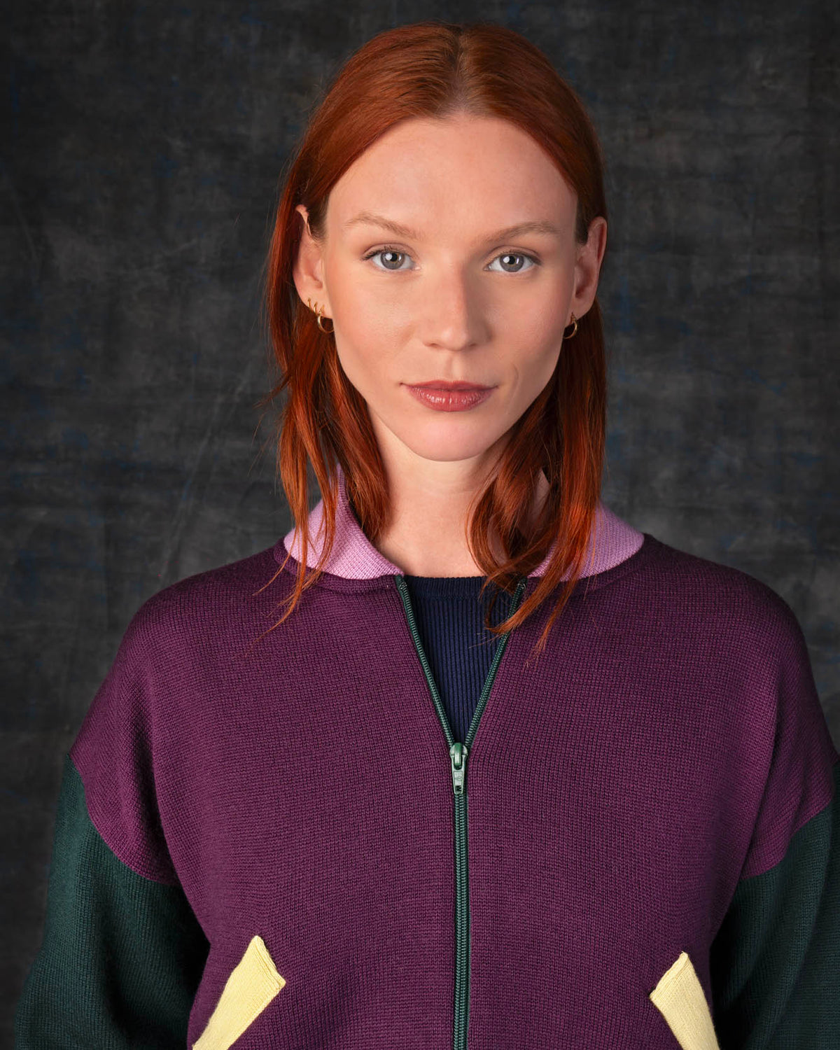 Close-up of a person wearing a grape purple zip-up bomber jacket with dark green sleeves and pink collar.