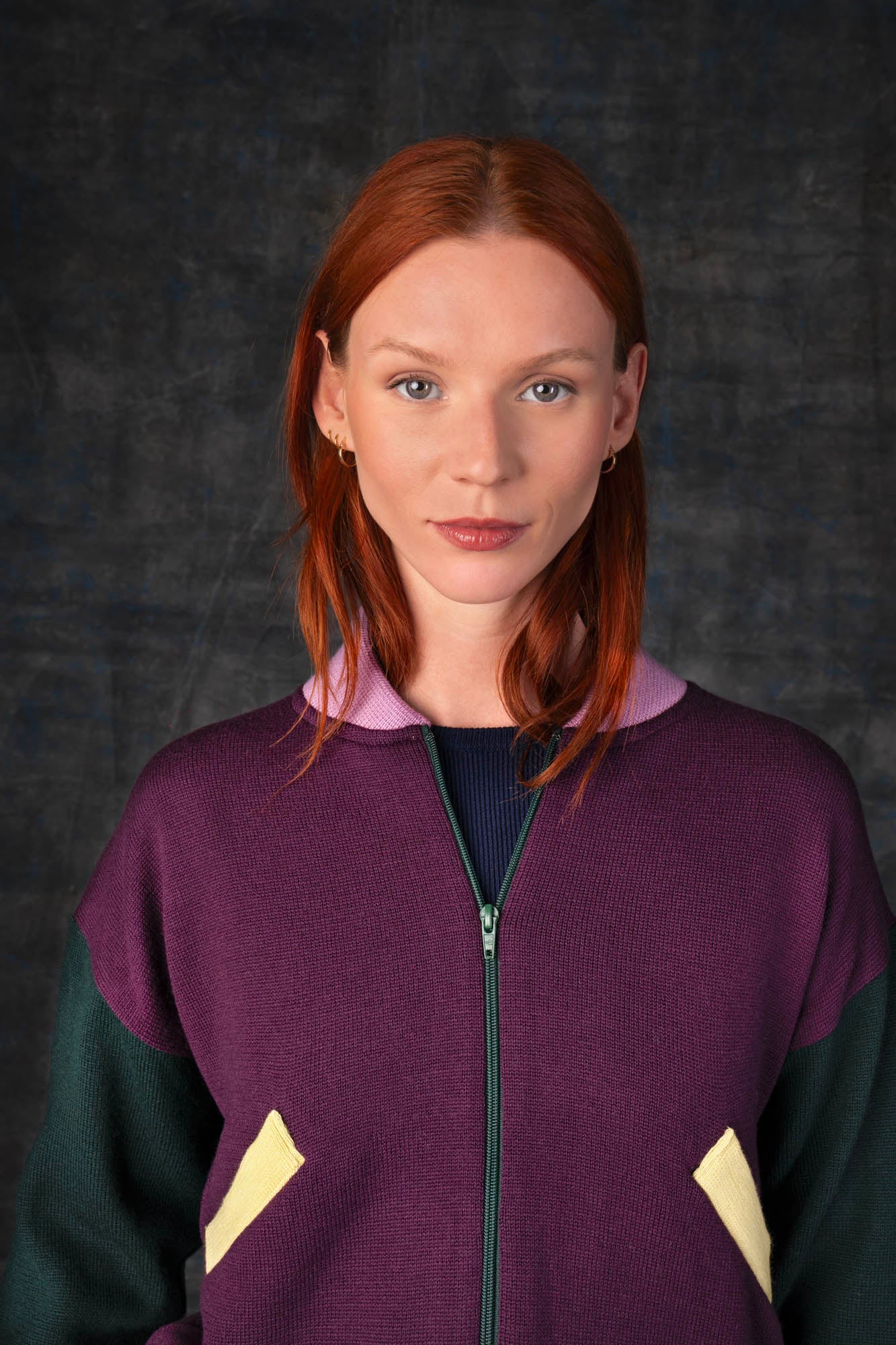 Close-up of a person wearing a grape purple zip-up bomber jacket with dark green sleeves and pink collar.