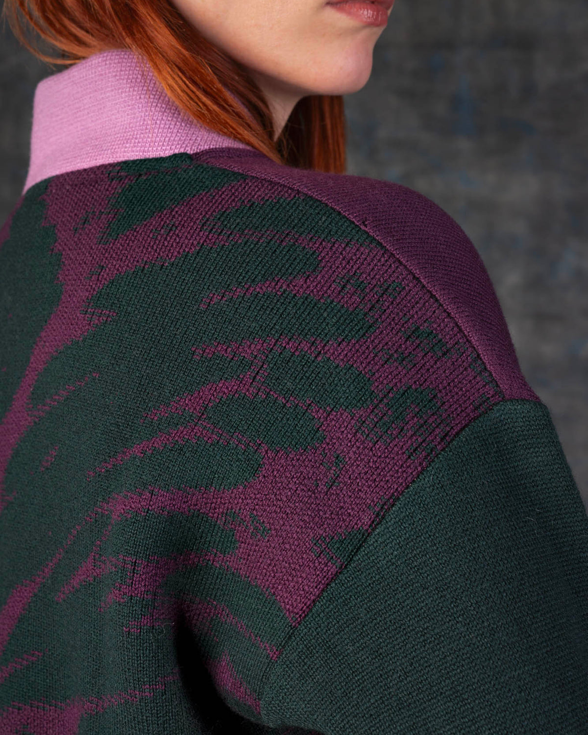 Close-up of a person wearing a grape purple bomber jacket with dark green sleeves and pink collar. There is an organic pattern inspired by a butterfly's wings on the back of the jacket.