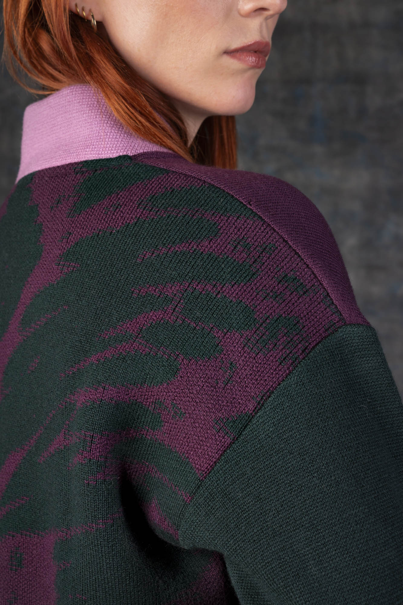 Close-up of a person wearing a grape purple bomber jacket with dark green sleeves and pink collar. There is an organic pattern inspired by a butterfly's wings on the back of the jacket.