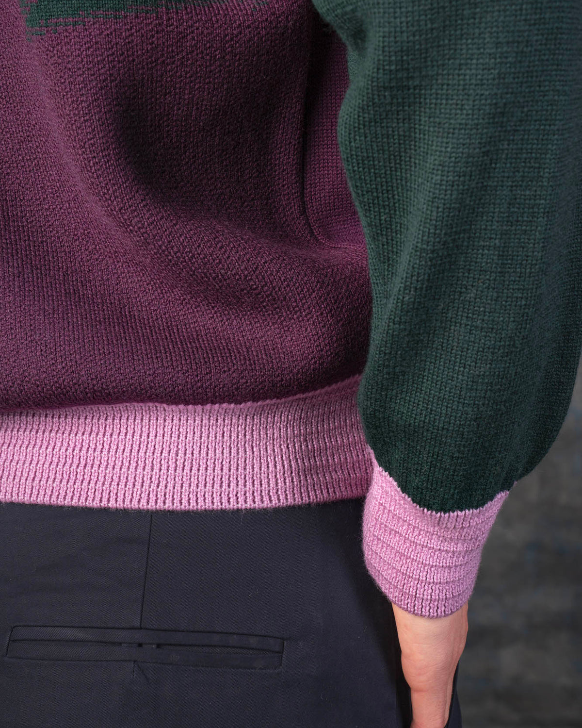 Close-up of a person wearing a grape purple bomber jacket with dark green sleeves and pink cuffs.
