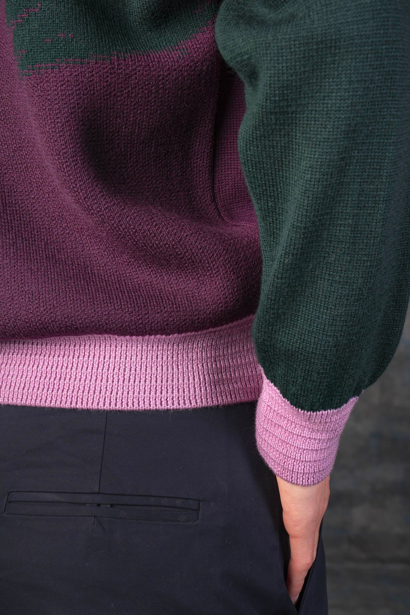 Close-up of a person wearing a grape purple bomber jacket with dark green sleeves and pink cuffs.