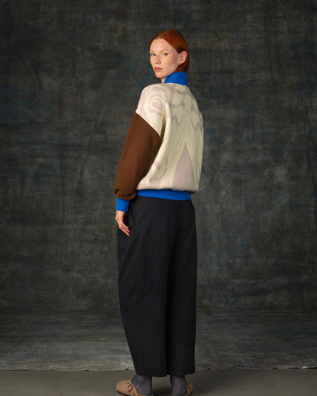 Female model wearing an ecru and brown bomber jacket with cobalt blue details. There is a subtle organic pattern inspired by a butterfly's wings on the back of the jacket.