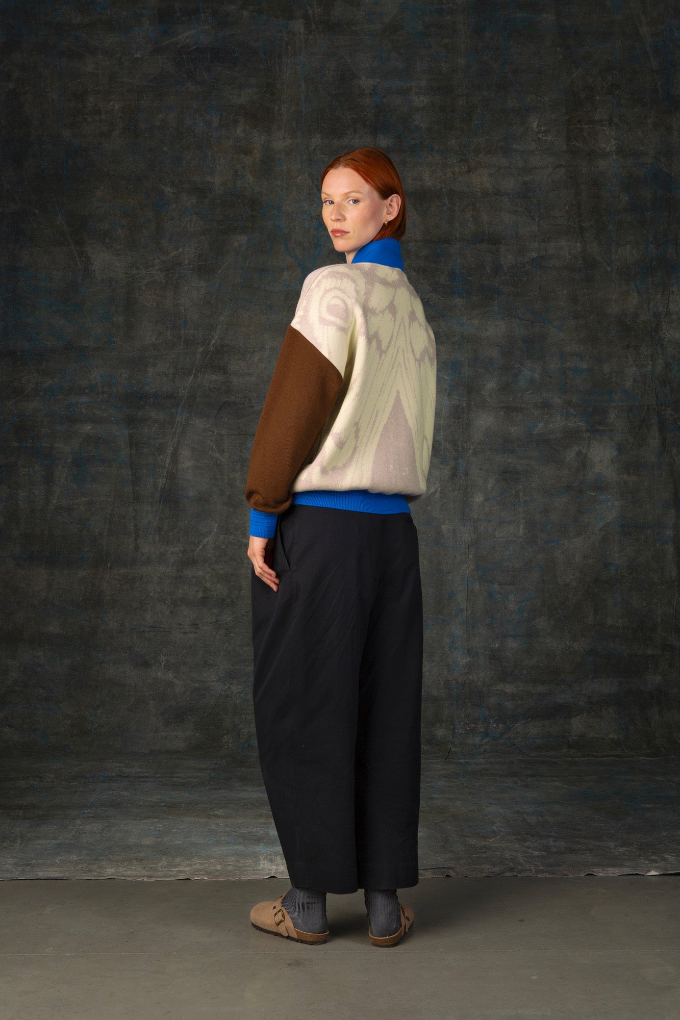 Female model wearing an ecru and brown bomber jacket with cobalt blue details. There is a subtle organic pattern inspired by a butterfly's wings on the back of the jacket.