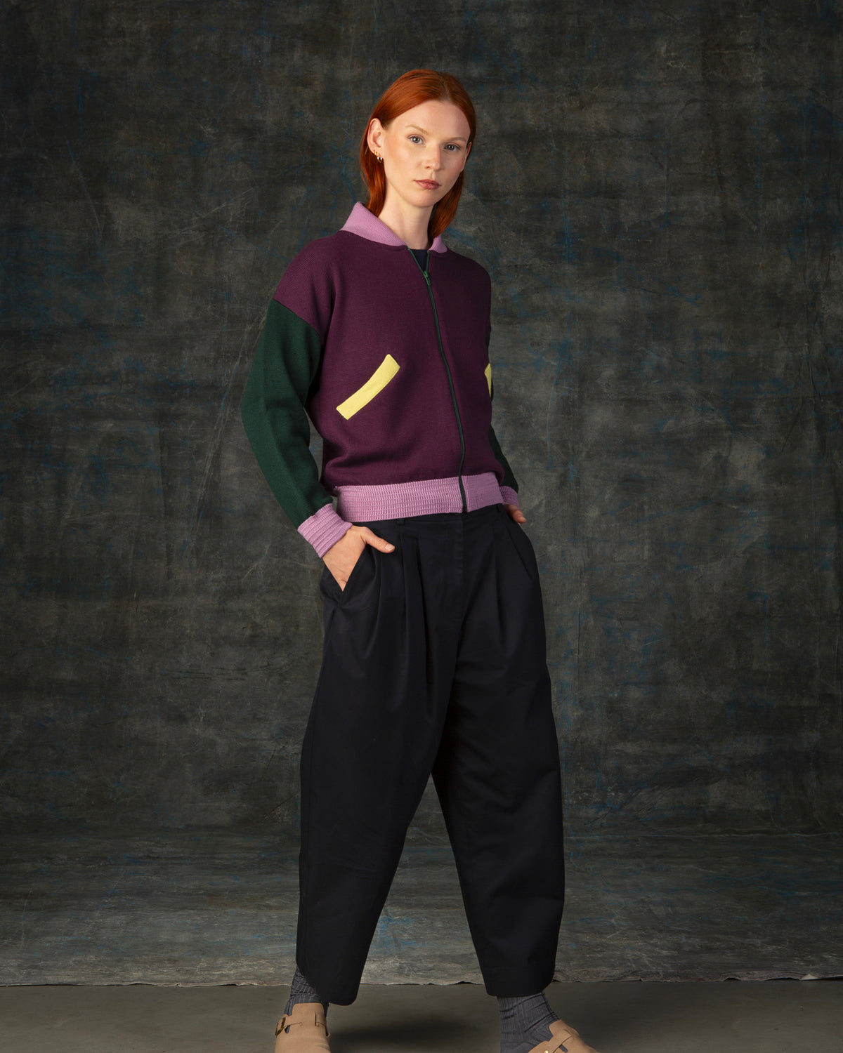 Female model wearing a grape purple zip-up bomber jacket with dark green sleeves and pink cuffs.