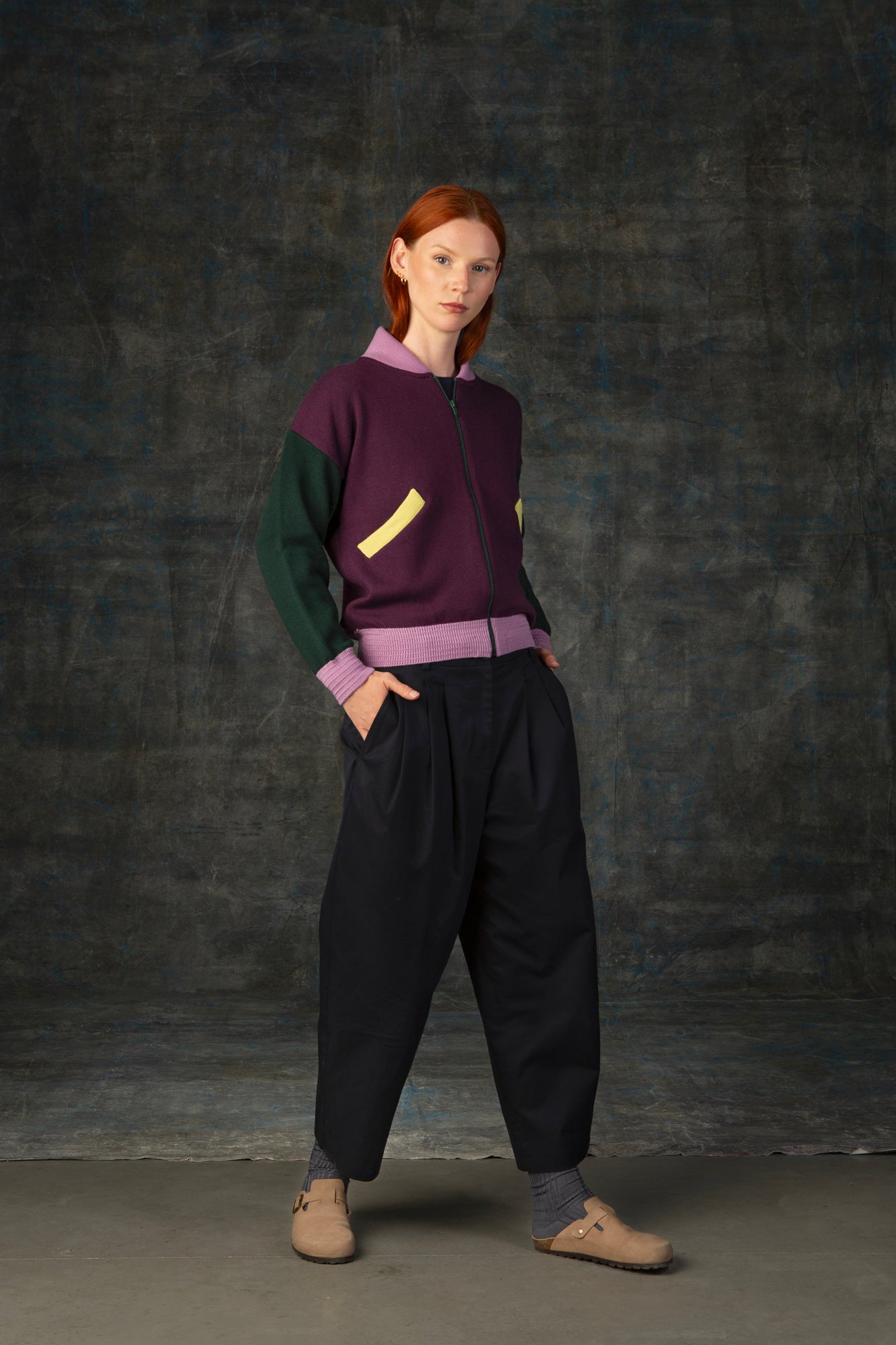 Female model wearing a grape purple zip-up bomber jacket with dark green sleeves and pink cuffs.