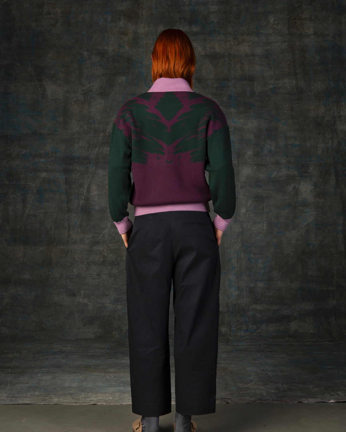 Female model wearing a grape purple bomber jacket with dark green sleeves and pink cuffs. There is an organic pattern inspired by a butterfly's wings on the back of the jacket.