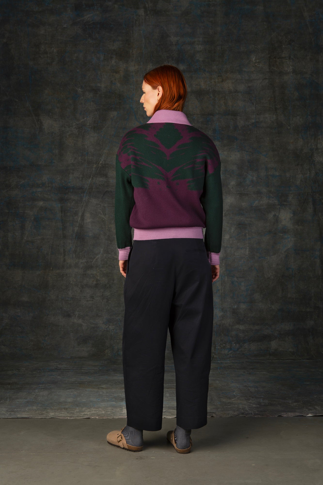 Female model wearing a grape purple bomber jacket with dark green sleeves and pink cuffs. There is an organic pattern inspired by a butterfly's wings on the back of the jacket.