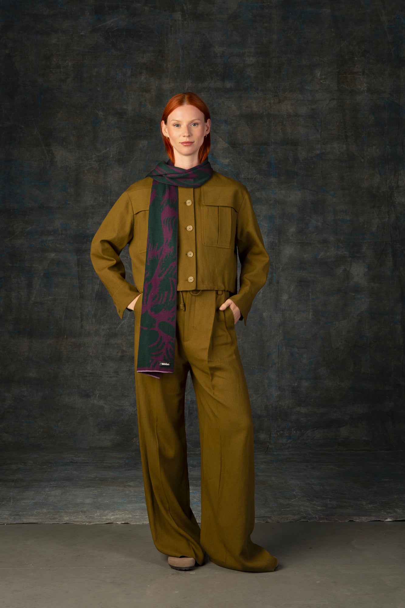 Female model wearing an olive green outfit with a purple and forest green midi scarf, with nature-inspired pattern, draped around her neck.