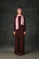Female model wearing a burgundy outfit with a mauve pink and beige scarf with an organic pattern, draped around her neck and matching pink headband.