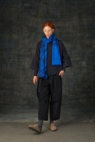 Female model wearing a dark blue outfit with a bright cobalt blue scarf, with nature-inspired pattern, draped around her neck.