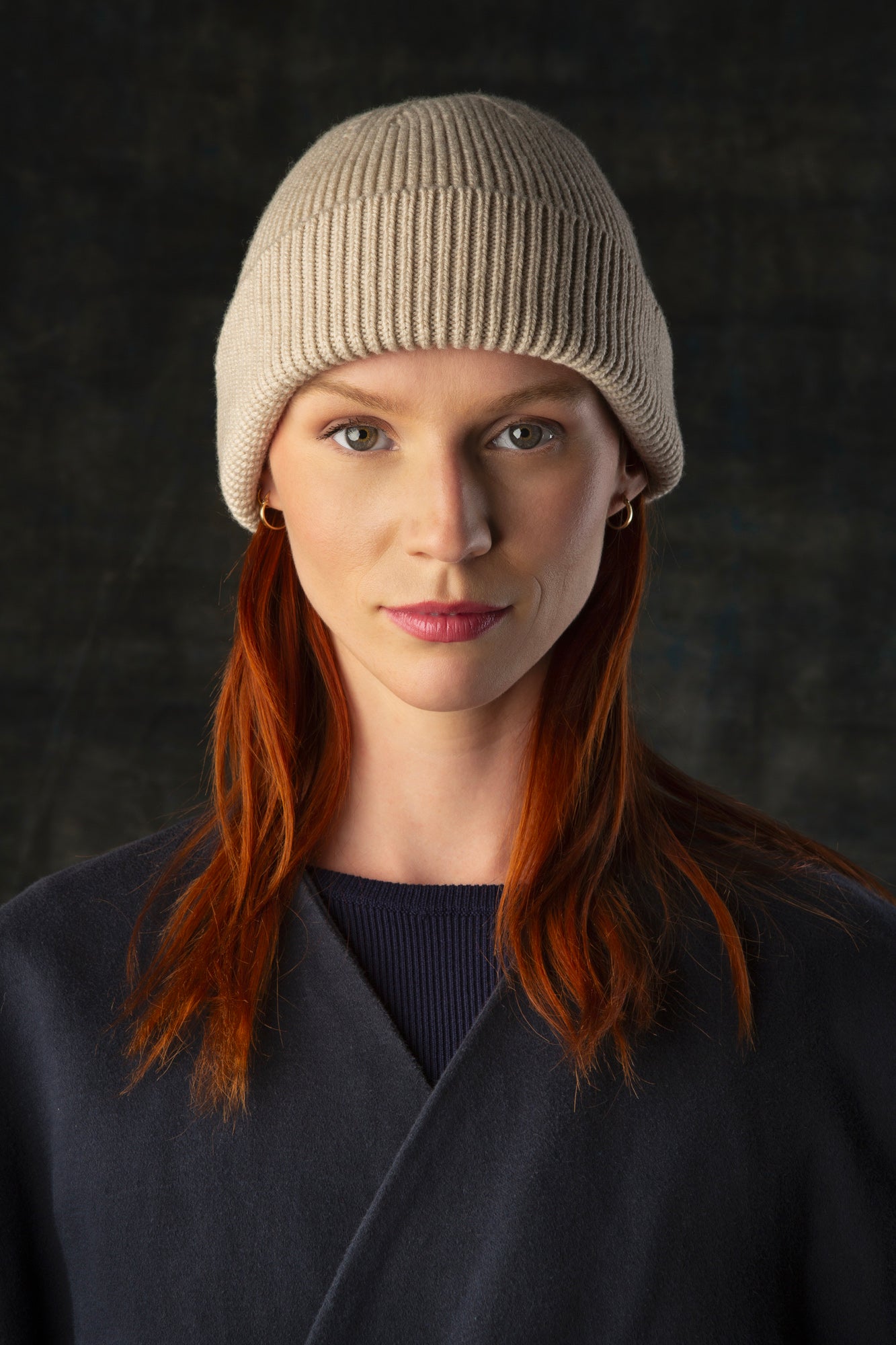 Person wearing an ecru knit beanie and dark blue coat against a dark background.