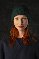 Person wearing a dark forest green knit beanie and dark blue coat against a dark background.