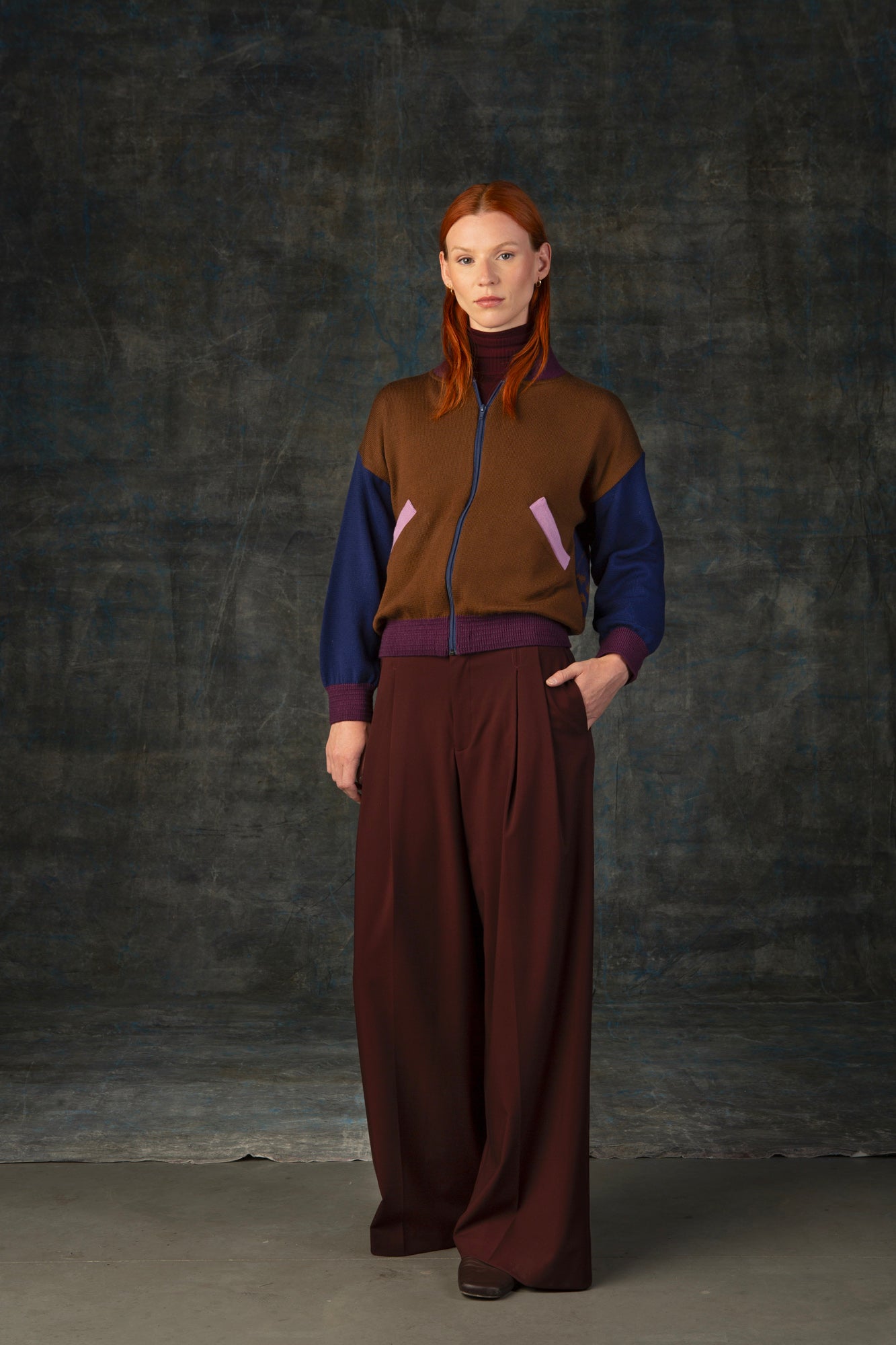 Female model wearing a cacao brown zip-up bomber jacket with dark blue sleeves and purple cuffs.