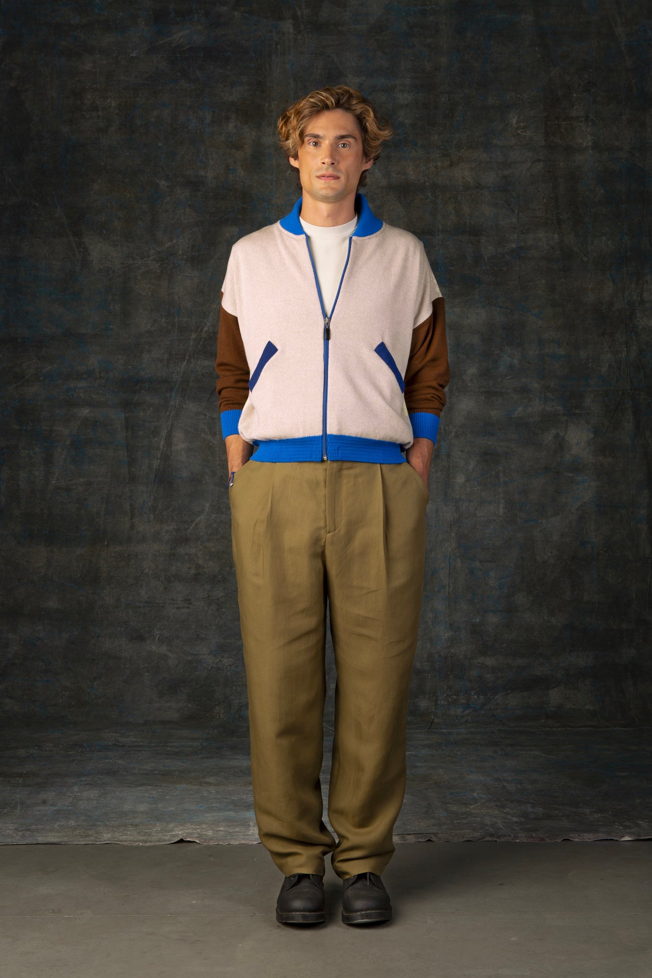 Male model wearing an ecru and brown zip-up bomber jacket with cobalt blue details. 