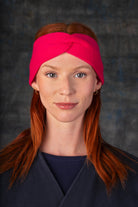 Person wearing a bright pink knit headband and dark blue coat against a dark background.