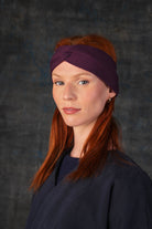 Person wearing a grape purple knit headband and dark blue coat against a dark background.