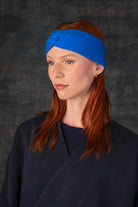 Person wearing a cobalt blue knit headband and dark blue coat against a dark background.