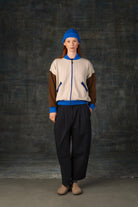 Female model  wearing an ecru and brown knit bomber jacket with cobalt blue details and matching cobalt blue beanie. 