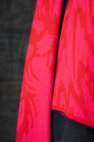 Close-up of a bright red and pink scarf with a nature-inspired pattern against a dark background.