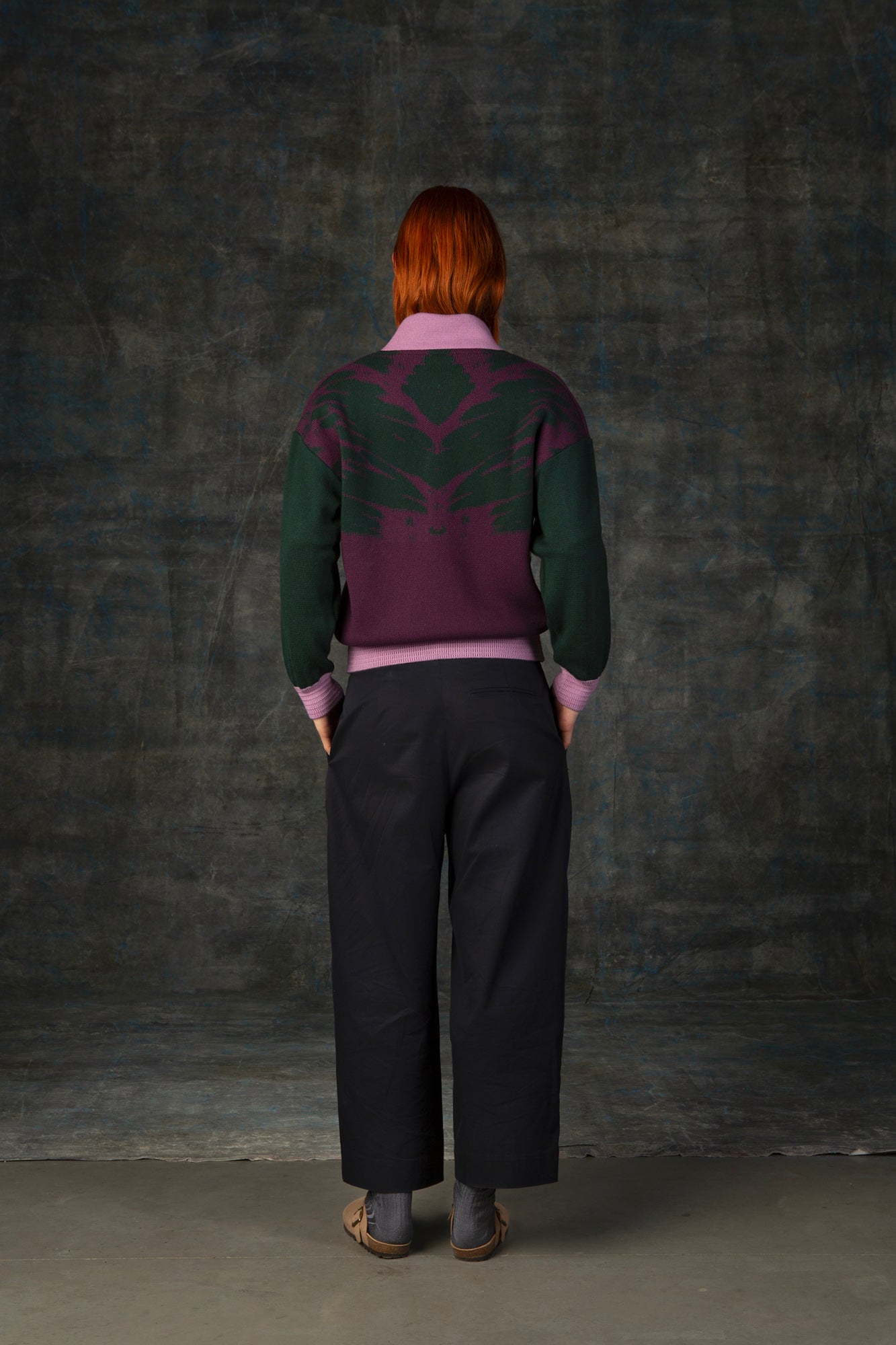 Female model wearing a grape purple bomber jacket with dark green sleeves and pink cuffs. There is an organic pattern inspired by a butterfly's wings on the back of the jacket.